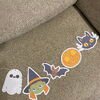Guirlande Halloween DIY posée sur un canapé : fantôme, sorcière, chauve-souris, citrouille et chat noir découpés, Loulou