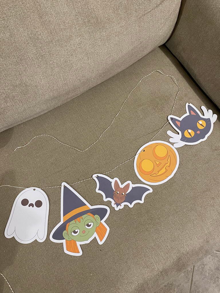 Guirlande Halloween DIY posée sur un canapé : fantôme, sorcière, chauve-souris, citrouille et chat noir découpés, Loulou